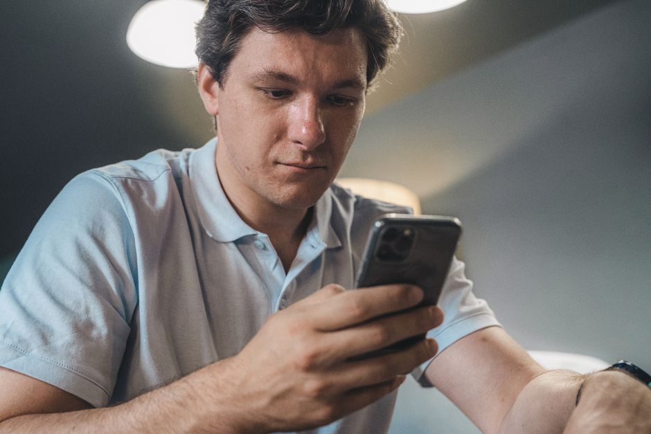 Adult man in casual attire intently using a smartphone indoors, focused and engaged.